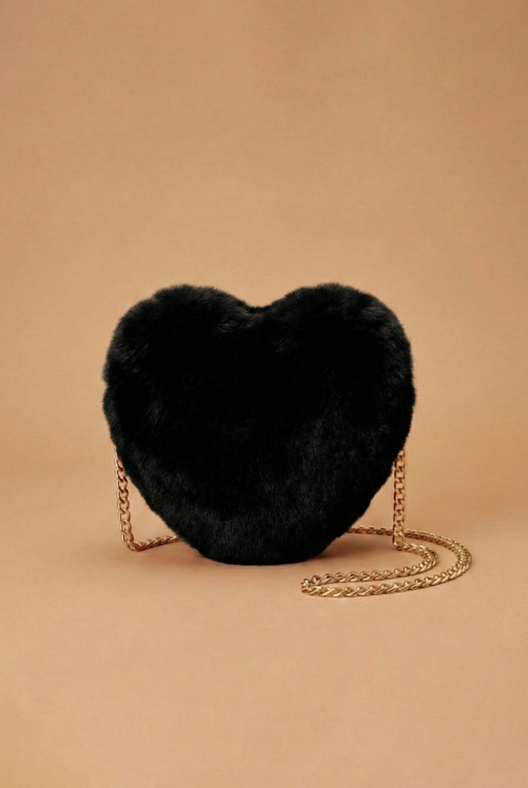 Black heart-shaped fur bag with a gold chain on a beige background