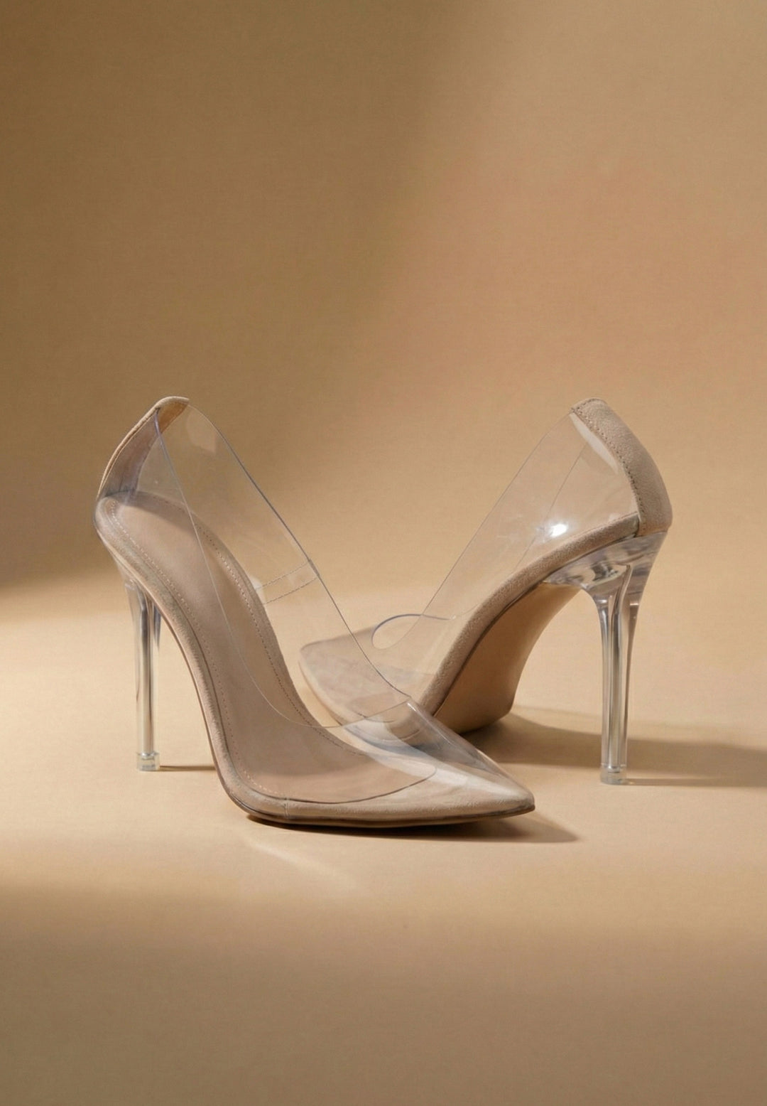 Pair of clear high-heeled shoes on a beige background